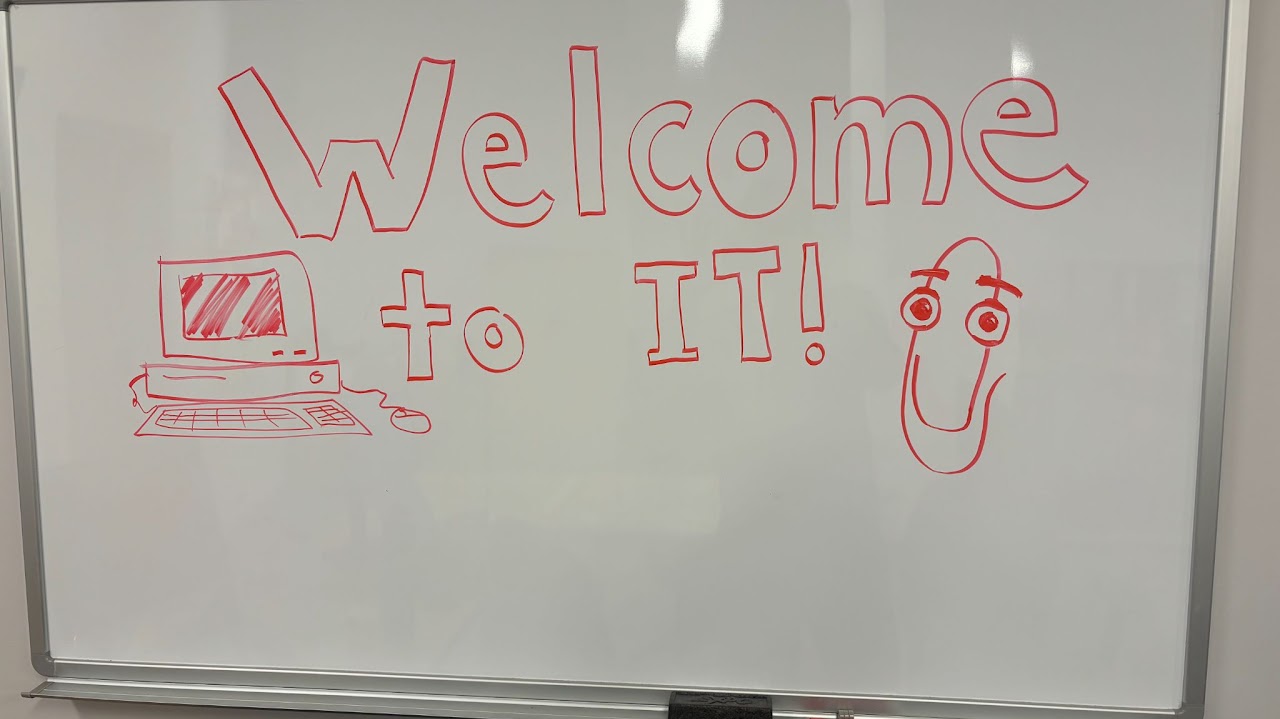 A whiteboard with the words "Welcome to IT!" and drawings of a computer and Clippy